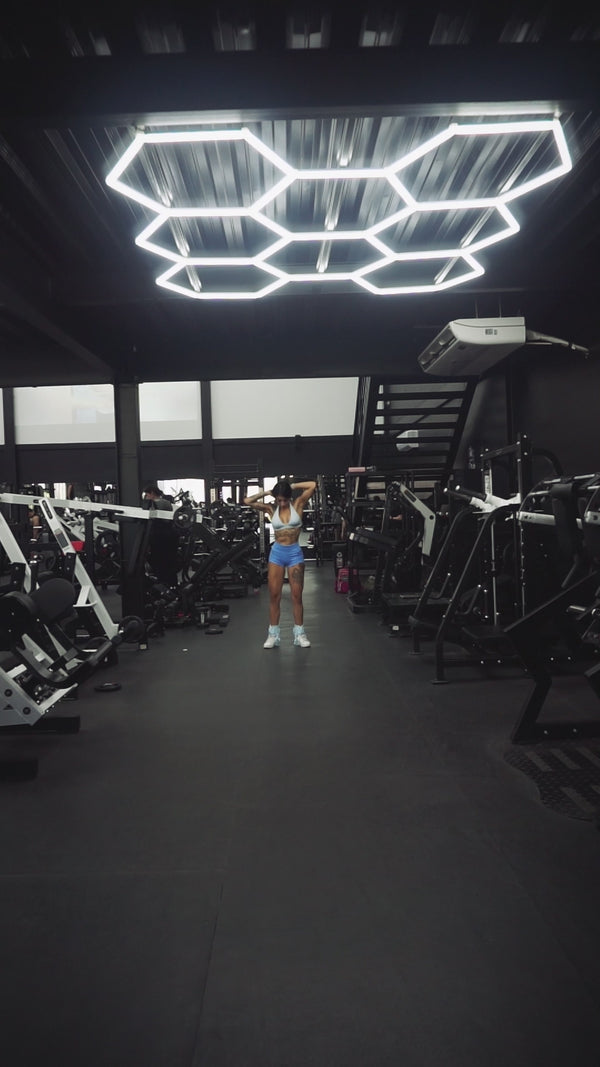 Mujer realizando sentadilla con barra en rack, ejercicio de fuerza para piernas y glúteos en gimnasio.
